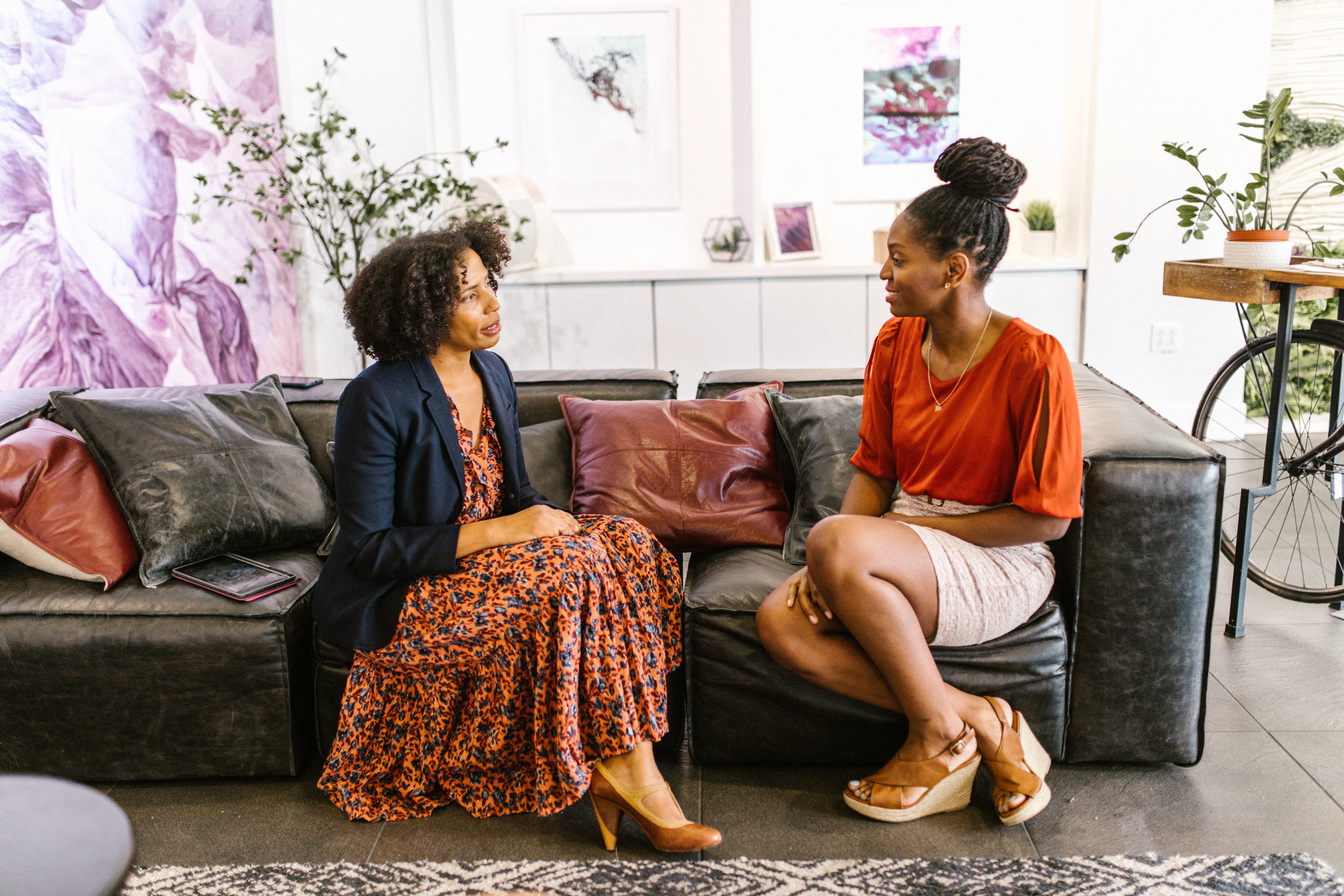 Women Sitting on a Black Leather Couch Having a Conversation